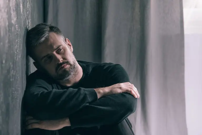 A man sitting against a wall, appearing distressed or deep in thought.