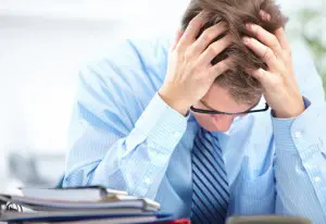 A person holding their head in frustration, surrounded by paperwork, implying stress or overwhelm.