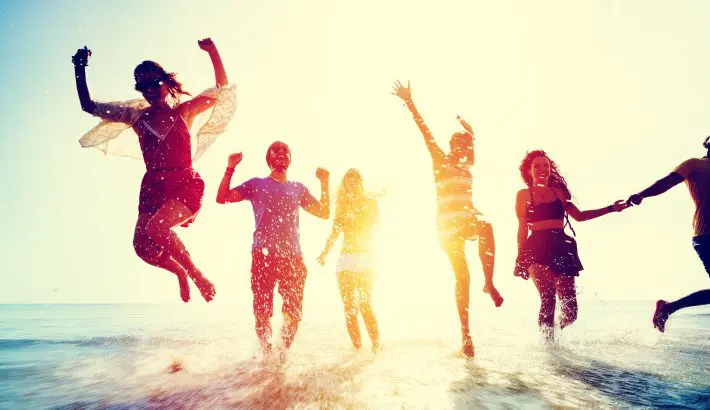 A joyful group is jumping at the beach against a bright, sunny backdrop.