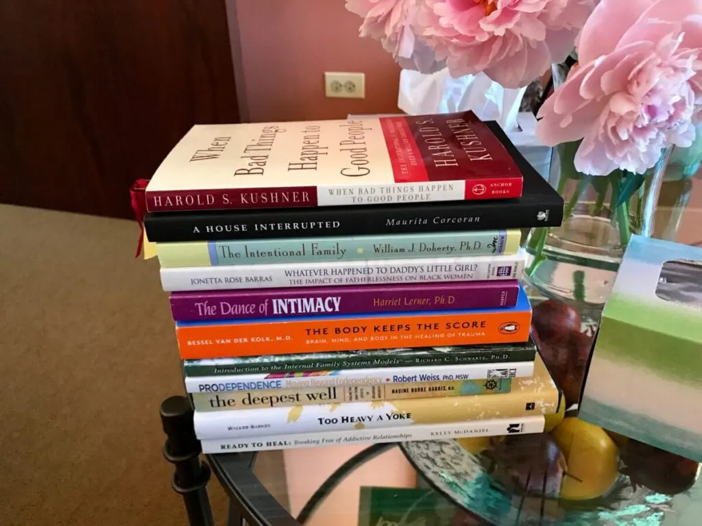 A stack of books on psychology, trauma, and family dynamics next to flowers and a tissue box.