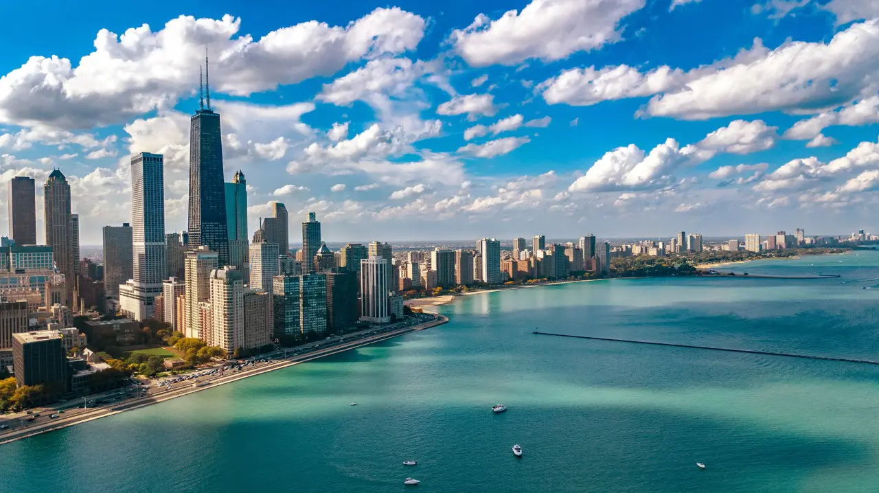 A city skyline with tall buildings by a large body of water under a partly cloudy sky.