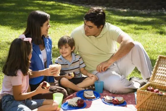 A family is enjoying a picnic in a park, sitting on a blanket with food and a basket.