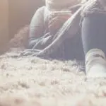 A person sits on a cozy rug, wrapped in a blanket, wearing socks. It's a calming scene, great for reflecting on how to stay positive during a job search.