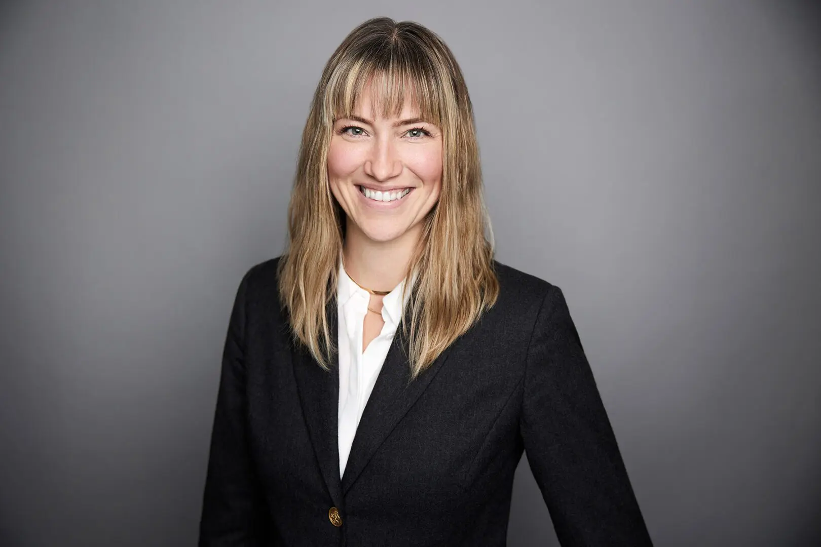 Smiling woman in professional attire, gray background.