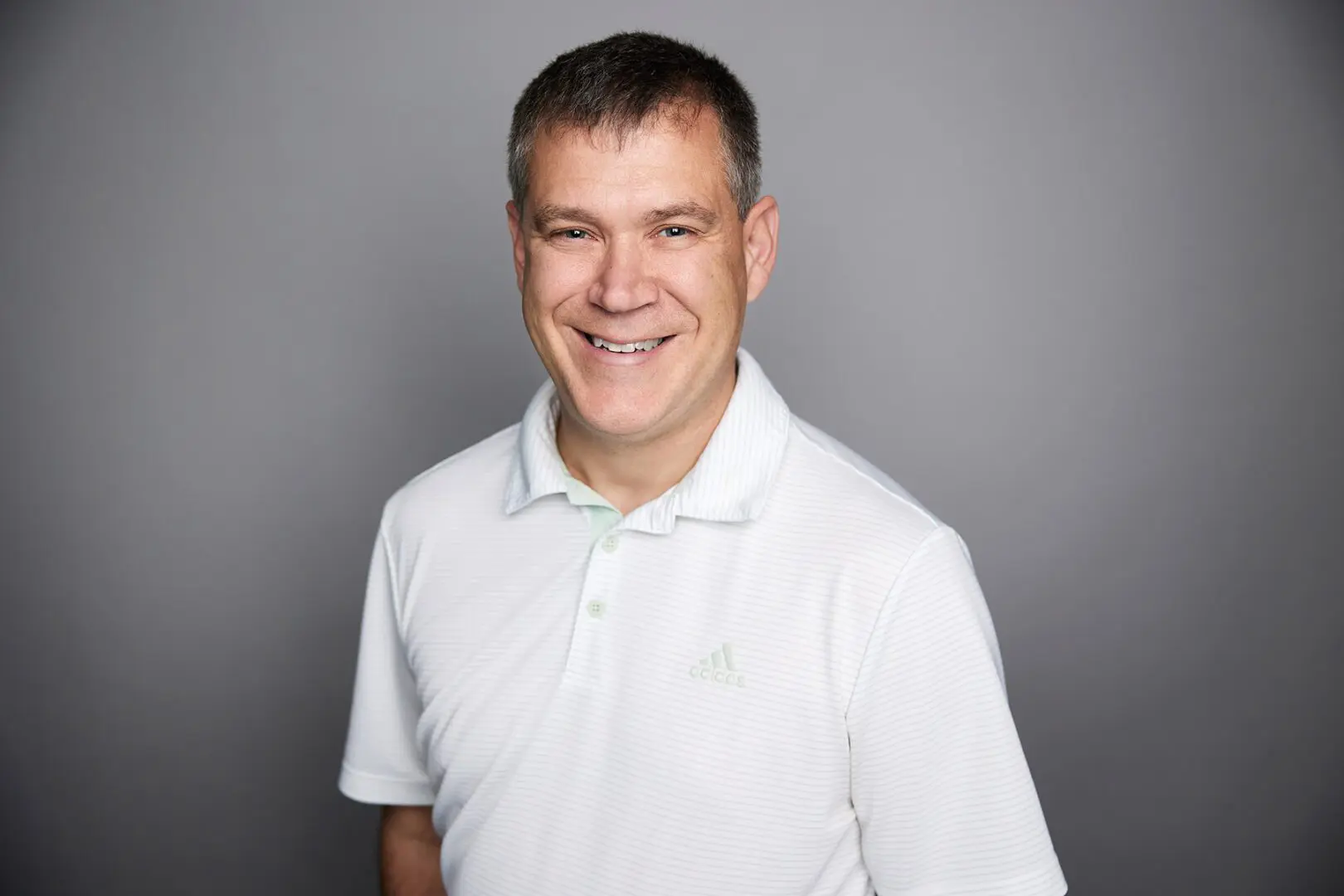 Smiling man in white shirt, gray background.