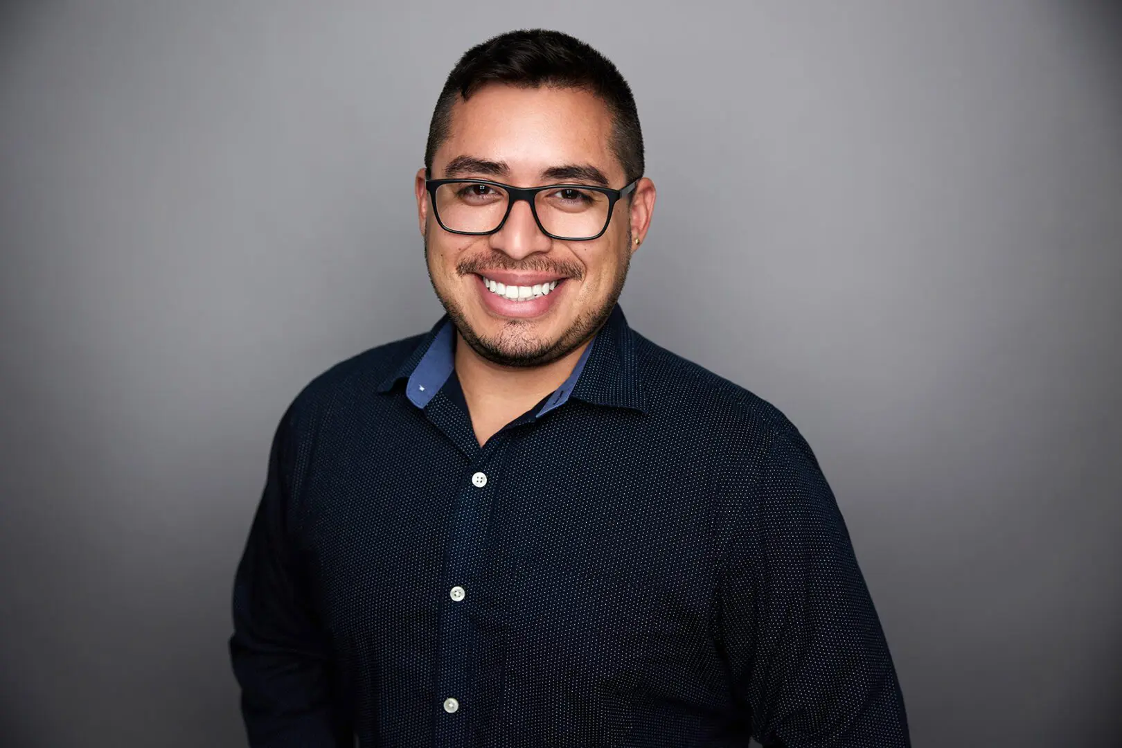 Smiling man wearing glasses and a dark shirt.