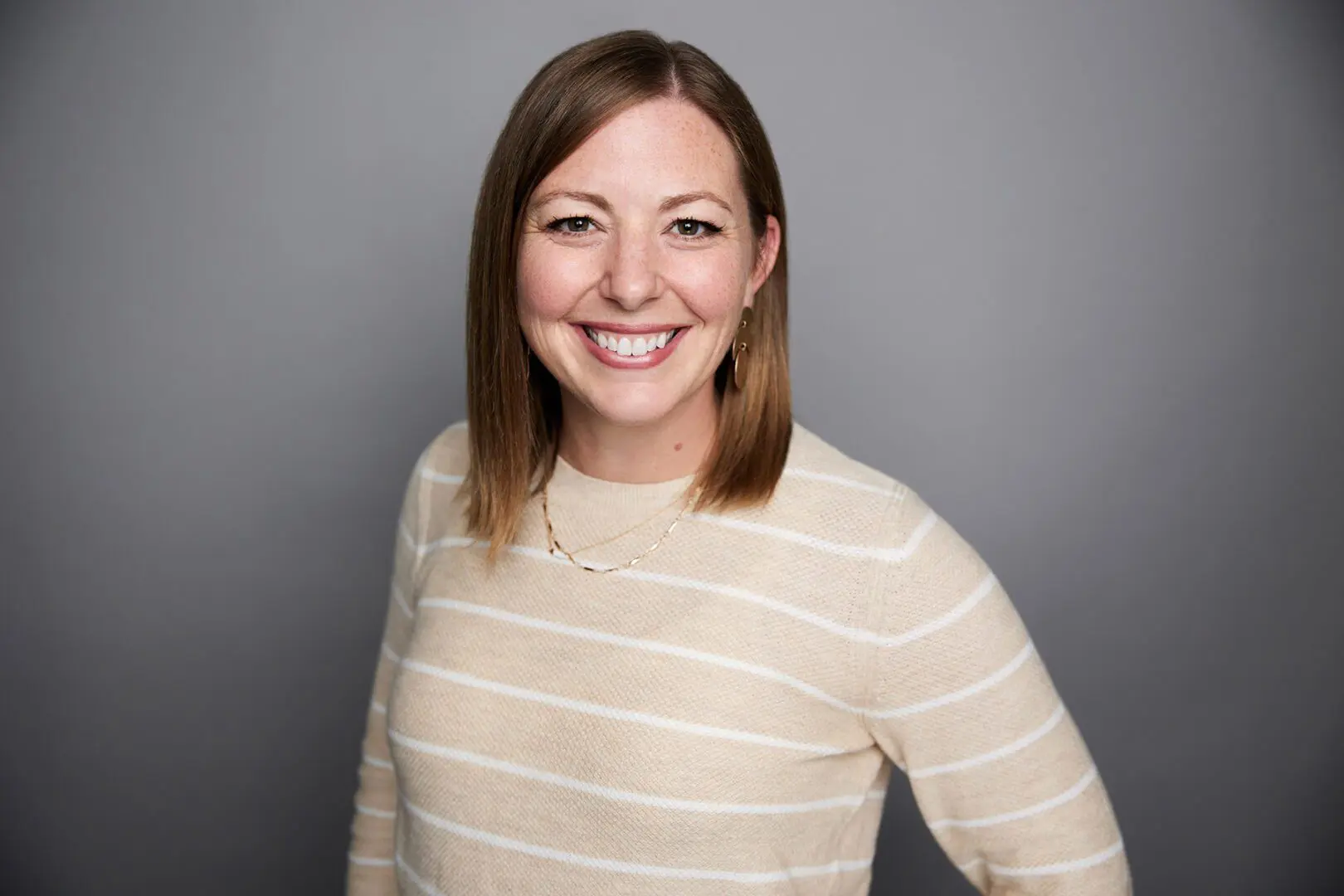 Smiling woman in a beige striped sweater.