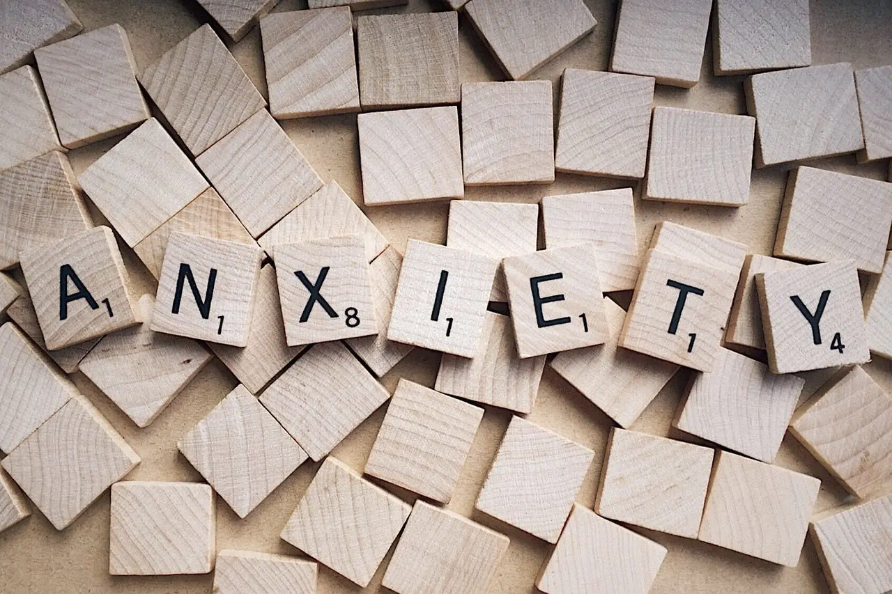 The word "ANXIETY" spelled out with Scrabble tiles on a scattered tile background.