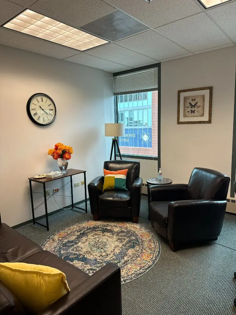 A cozy office with leather chairs, a patterned rug, a clock, and a lamp.