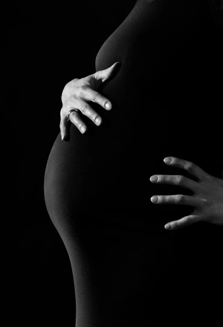 A close-up, black and white photo of a pregnant belly with hands gently resting on it.