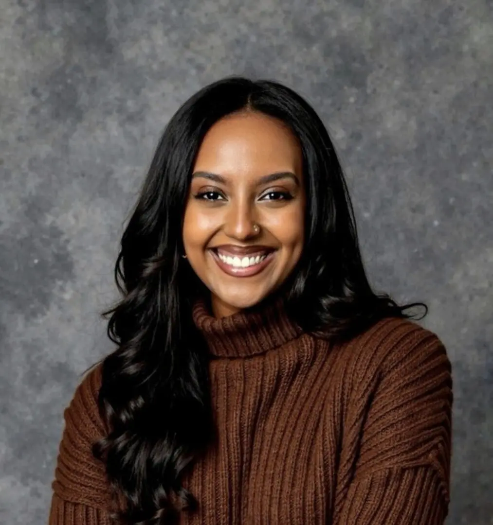 Smiling woman in a brown sweater against a gray backdrop.