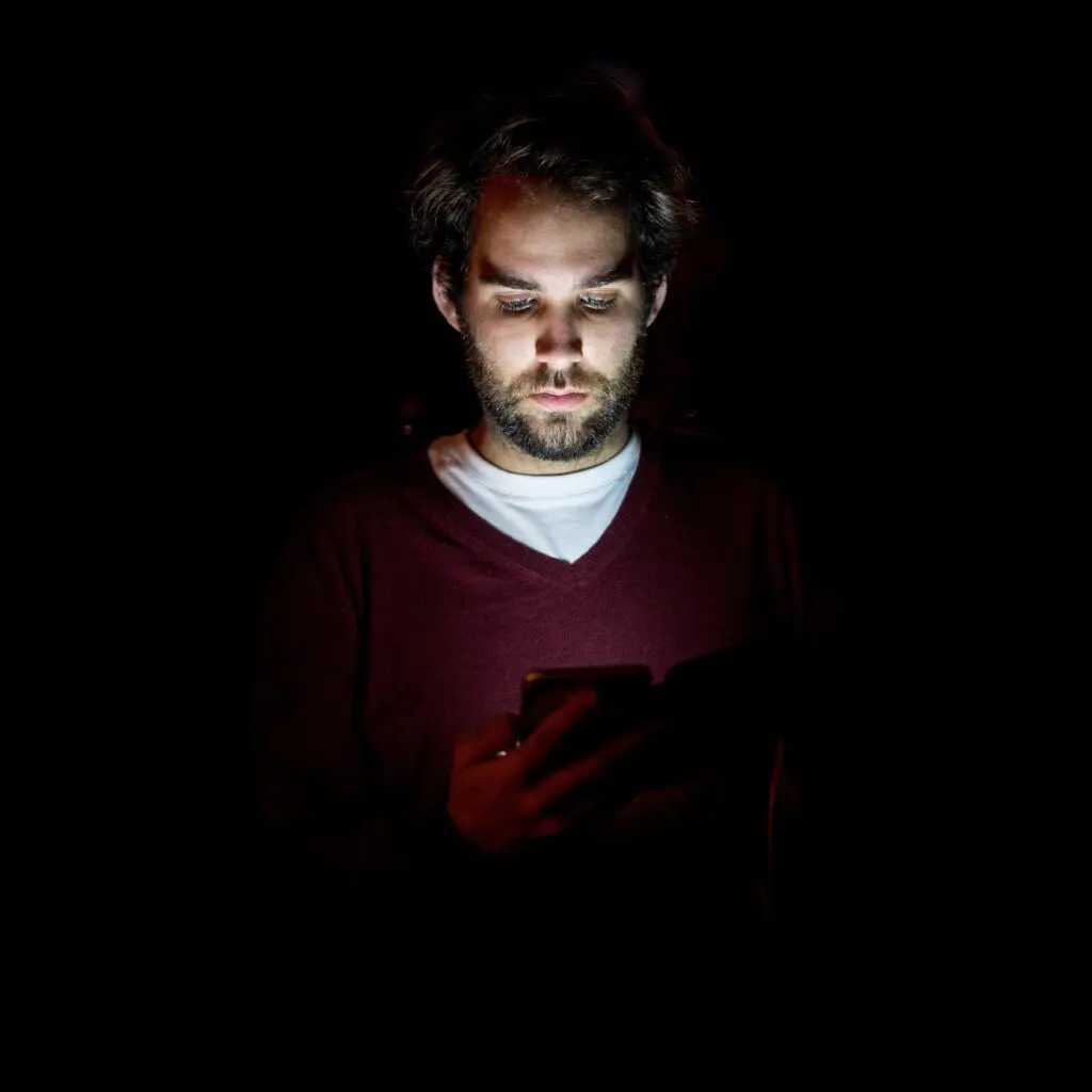 A man is illuminated by a phone screen in the dark. Feeling lonely may be a keyword.