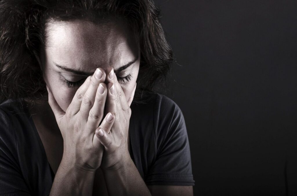 A person appears distressed, with their hands covering their face, possibly indicating stress or sadness.