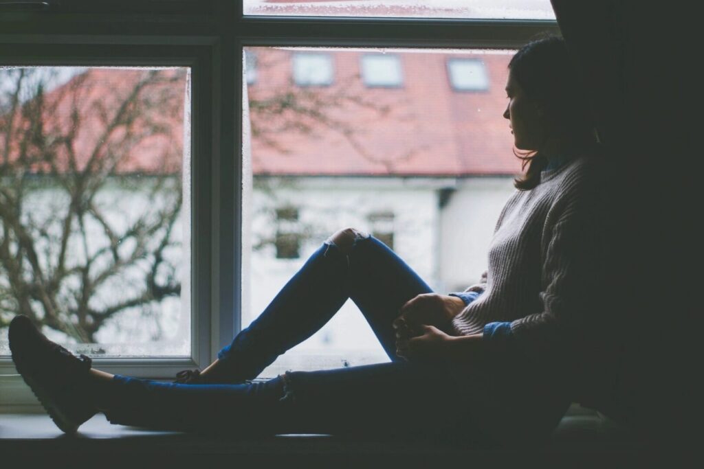A person sits on a windowsill, gazing outside at a blurred landscape.