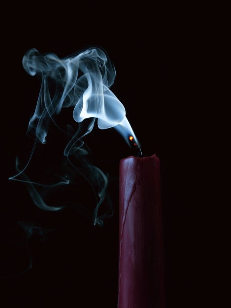Smoke rising from a recently extinguished candle against a dark background.