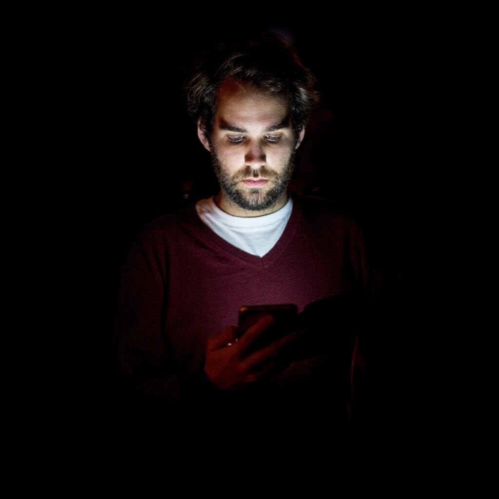 Man illuminated by phone light in dark surroundings.