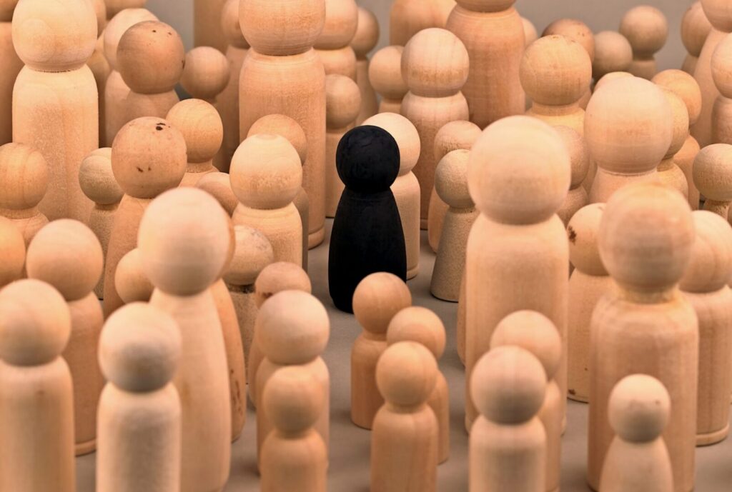 Black figurine among natural wooden peg dolls