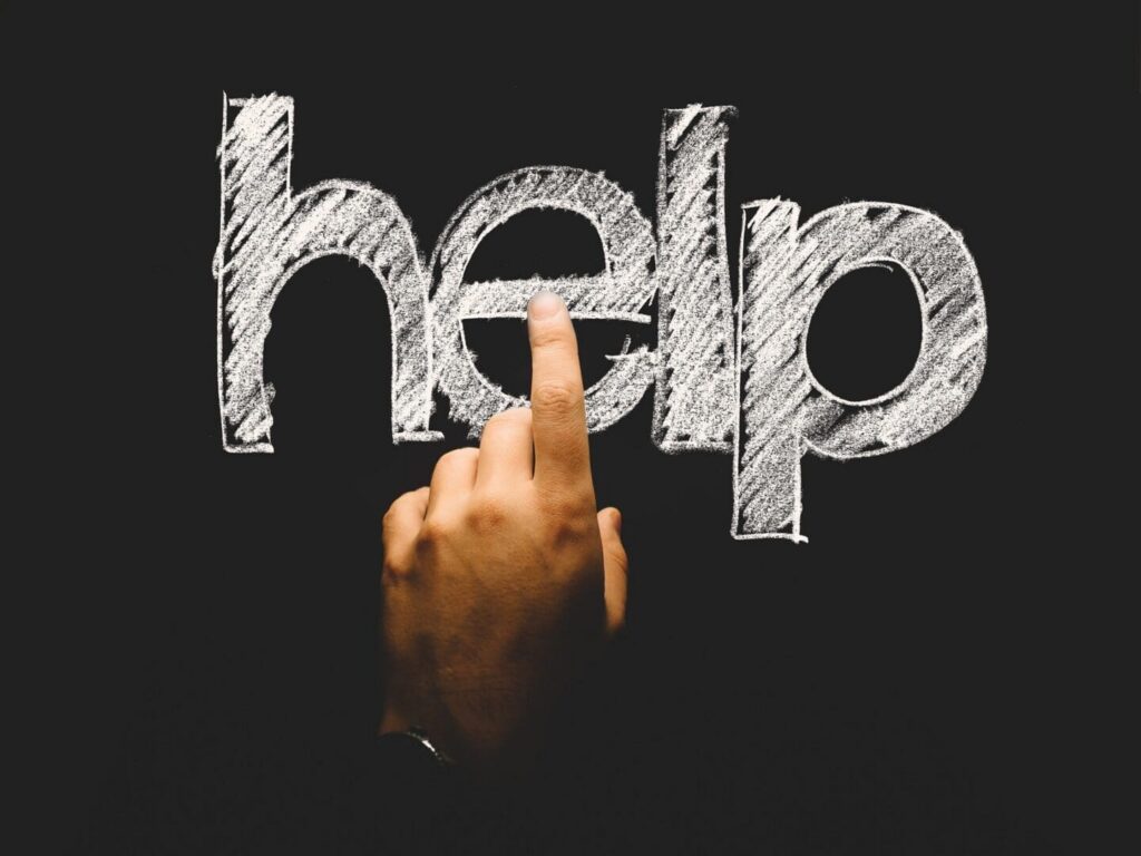 Hand pointing at chalk "help" on blackboard