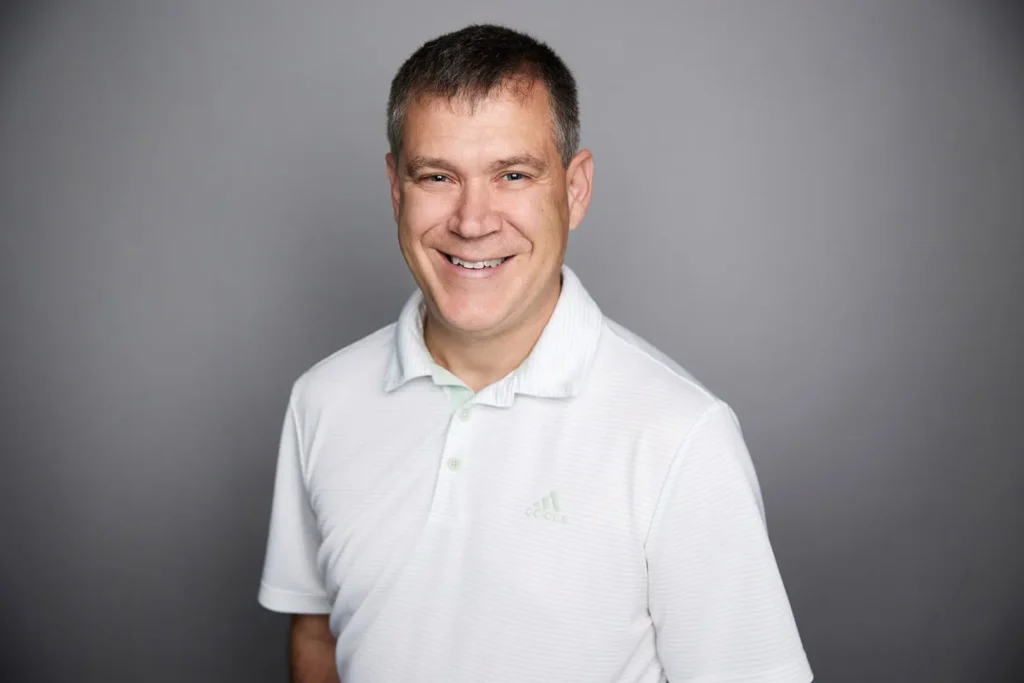Smiling man in white shirt, gray background.