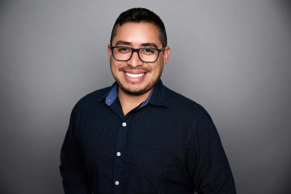Smiling man wearing glasses and a dark shirt.