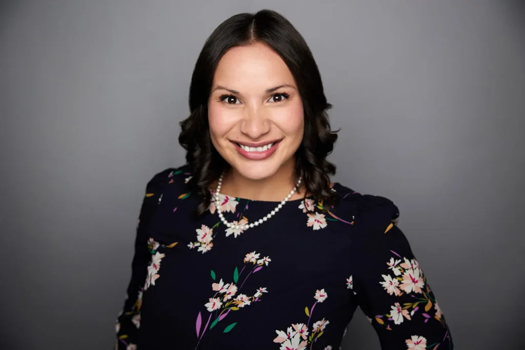 Smiling woman in floral dress, grey background.
