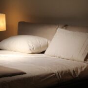 A cozy bedroom with white pillows and sheets, softly lit by a bedside lamp.