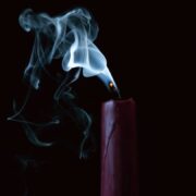 Smoke rising from a recently extinguished candle against a dark background.