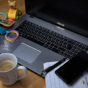 Laptop, coffee, toys, and phone on desk.